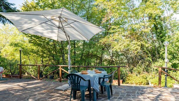 A stone patio with a table and chairs, an umbrella, and a wooden railing. - Vacation Home "Il Colletto Romantic Stonehouse" with Mountain View, Garden & Terrace (Pescia)