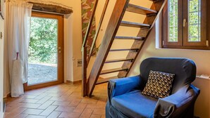 A room with a wooden staircase, a blue armchair, and a door leading outside. - Vacation Home "Il Colletto Romantic Stonehouse" with Mountain View, Garden & Terrace (Pescia)