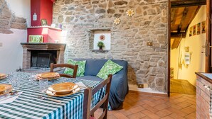A stone-walled room with a fireplace, a sofa, a dining table set with plates and glasses, and a red accent wall. - Vacation Home "Il Colletto Romantic Stonehouse" with Mountain View, Garden & Terrace (Pescia)