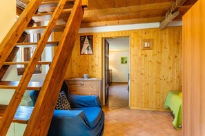 Un intérieur en bois avec un escalier, un canapé, une petite table et une porte donnant sur une autre pièce.