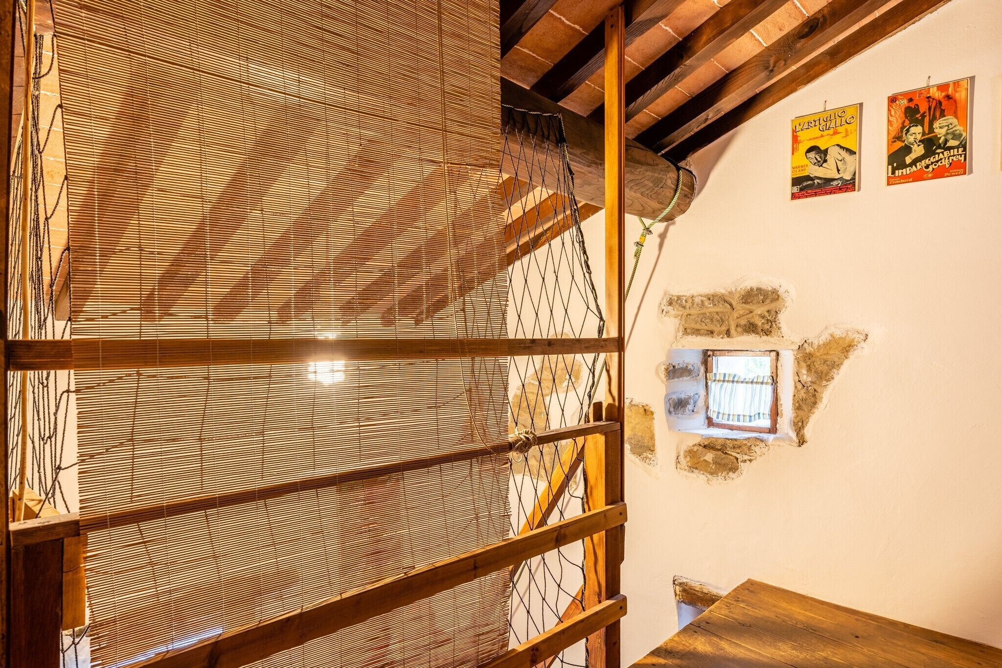 A rustic room with a wooden ceiling, a window with a view, and a wall with posters.