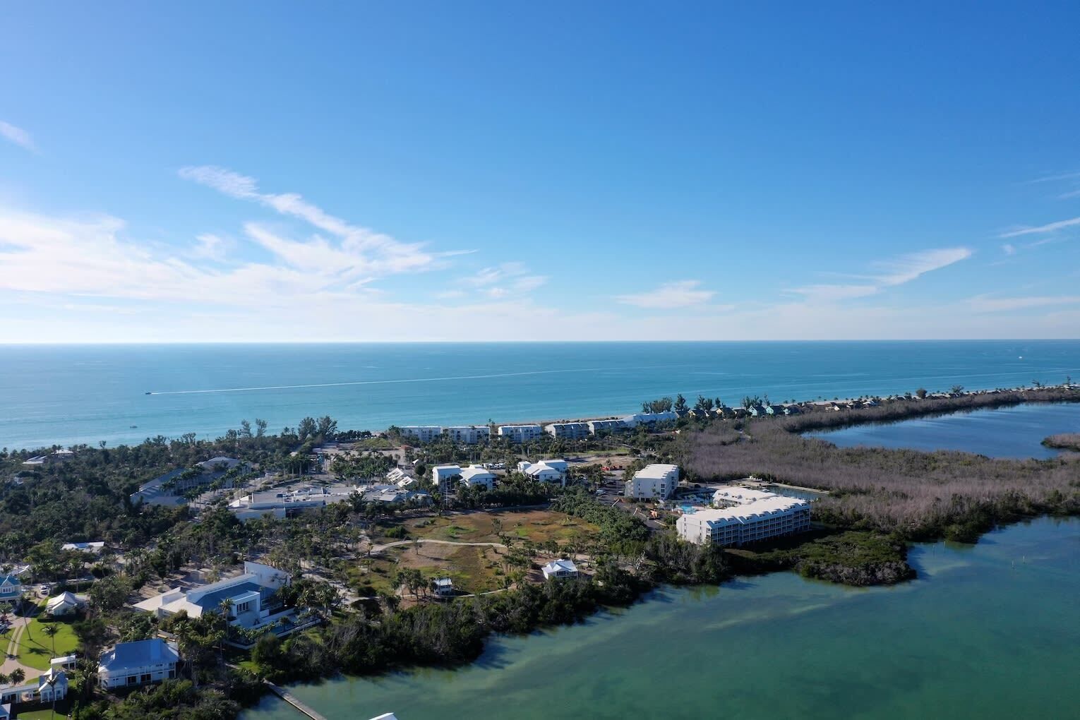 An aerial view of a coastal resort with multiple buildings, a marina, and a clear view of the ocean.