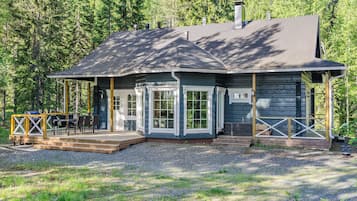 A cabin with a deck, large windows, and a chimney.