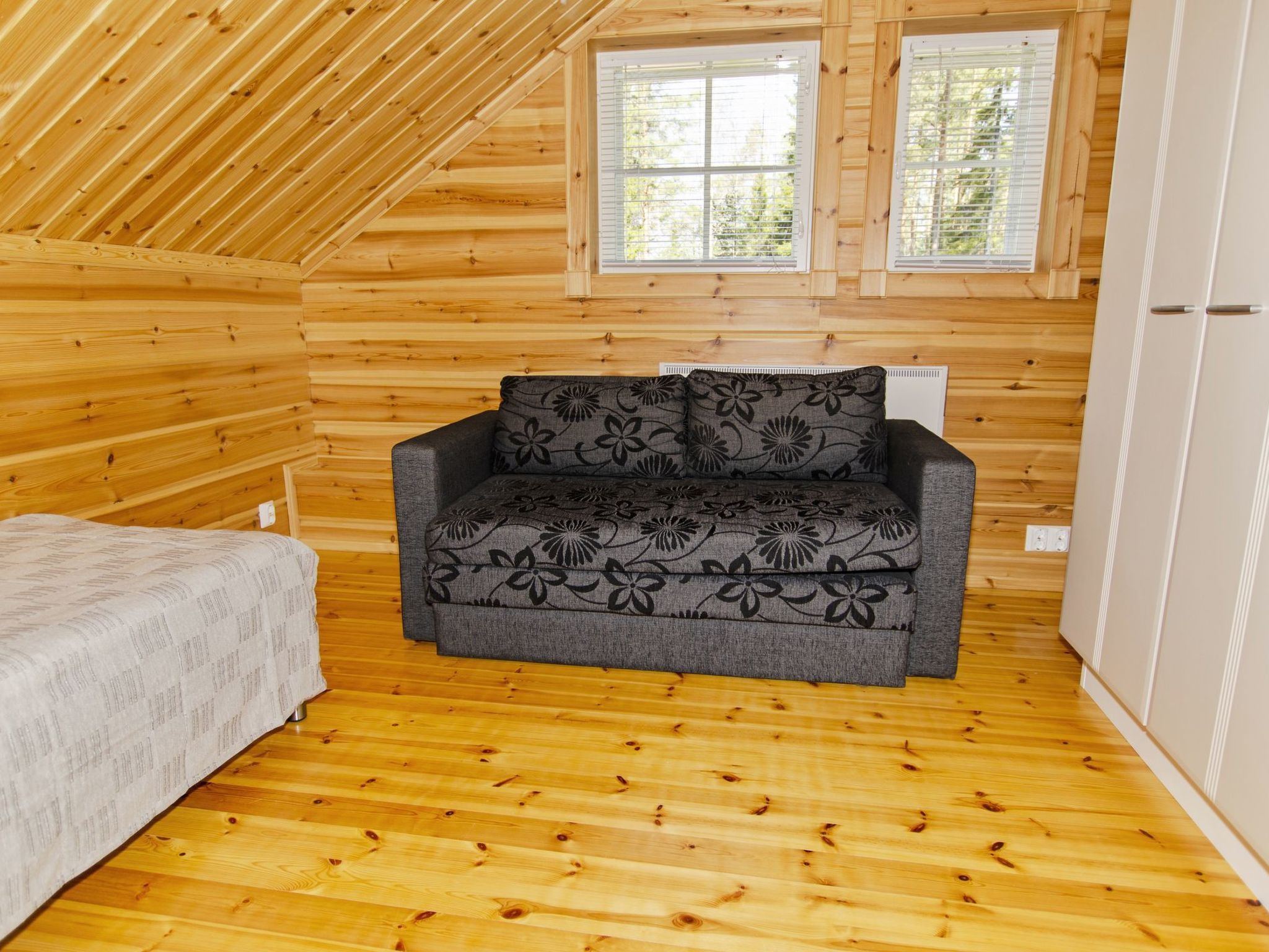 Una habitación acogedora con techo inclinado, paredes de madera, un sofá estampado con motivos florales y una cama con colcha estampada.