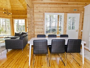 L’intérieur d’un chalet en bois comprend une table à manger, quatre chaises, un canapé et de grandes fenêtres.