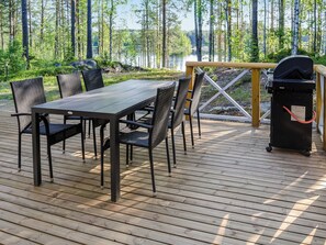 En træterrasse med et bord og stole, grill og udsigt til skov og sø.