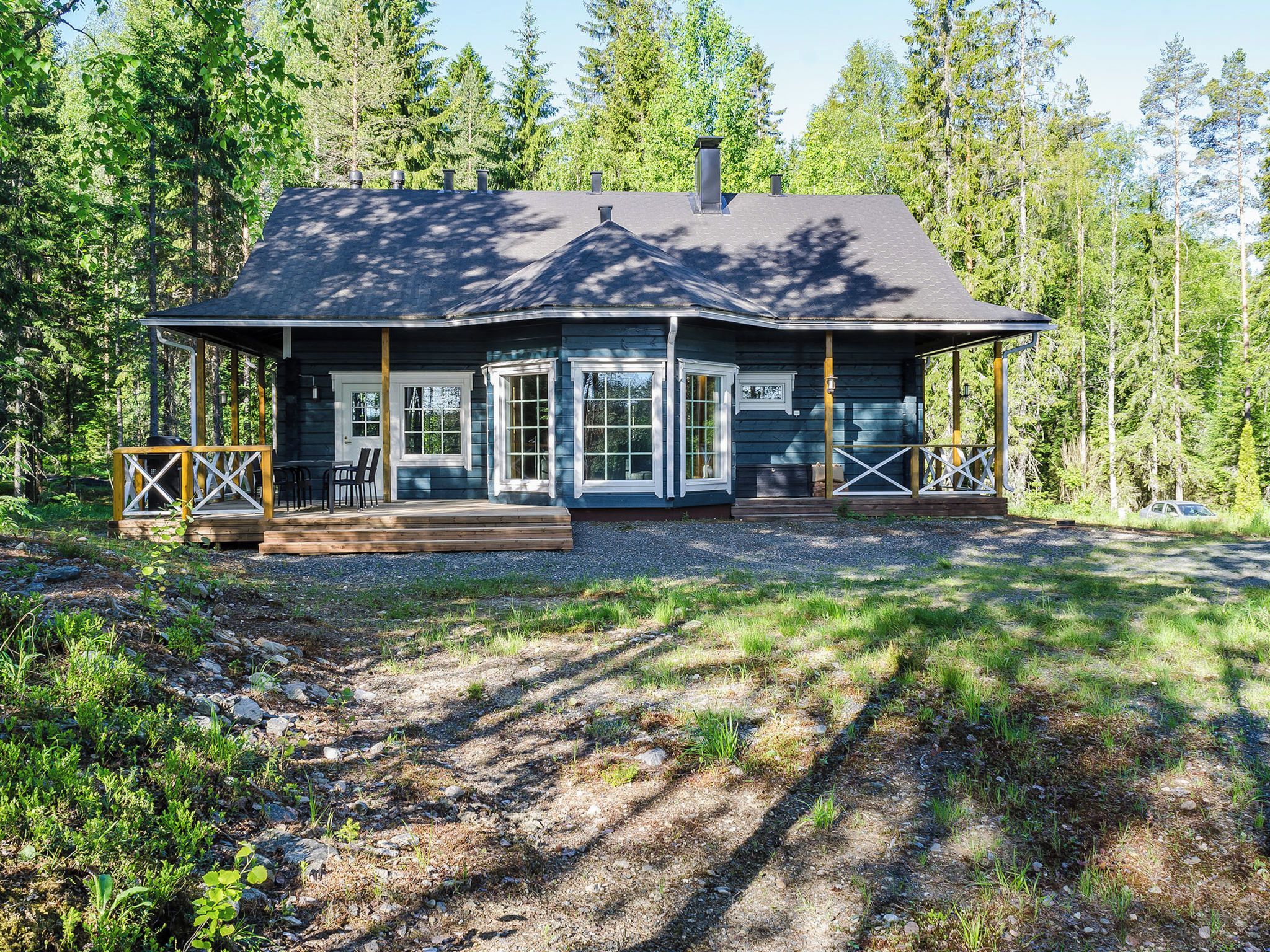A cabin with a covered porch, a chimney, and a gravel driveway.