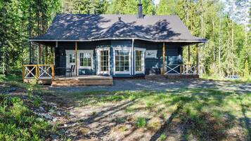 A cabin with a covered porch, a chimney, and a gravel driveway.