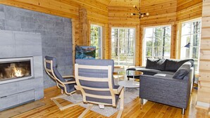 L’intérieur chaleureux d’un chalet avec une cheminée, des murs en bois et de grandes fenêtres donnant sur la forêt.