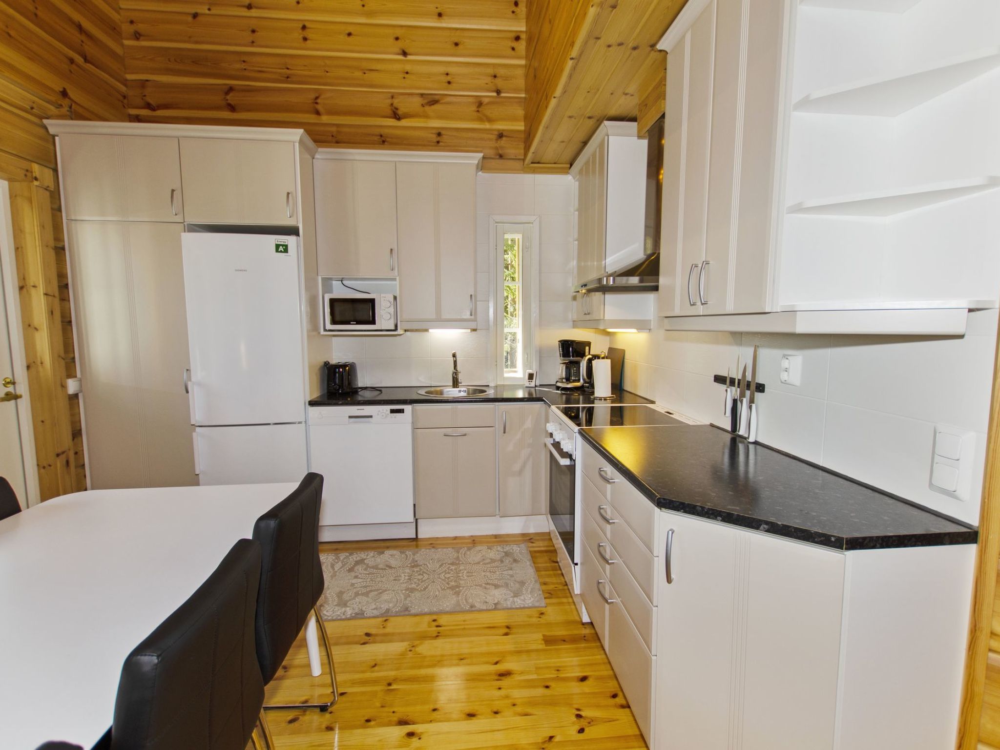 Una cocina compacta con gabinetes blancos, microondas, pileta y estufa.