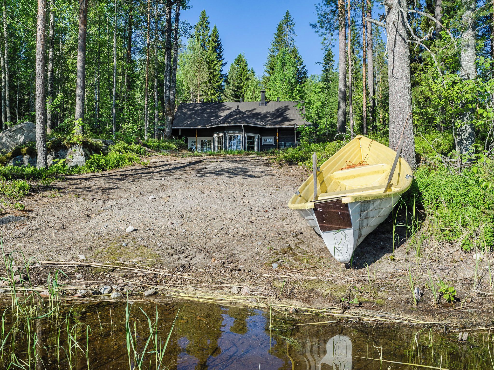 A cabin in a forest with a boat on a muddy shore.