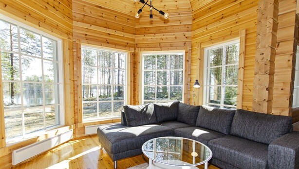 L’intérieur chaleureux d’un chalet avec un canapé d’angle, une table basse en verre et de grandes fenêtres donnant sur la forêt.