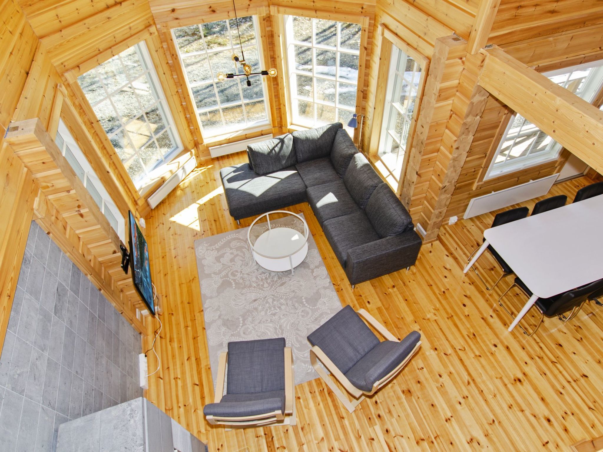 Eine Holzhütte mit einem großen Fenster, einer Couch, zwei Sesseln und einem kleinen runden Tisch.
