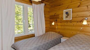 Quarto com duas camas, janela com cortinas, luminária de parede e um quadro emoldurado.