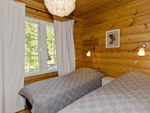 Une chambre avec deux lits, une fenêtre avec des rideaux, une lampe fixée au mur et un tableau encadré.