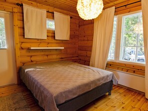 Een slaapkamer in een houten hutje, met een bed, gordijnen en een raam.