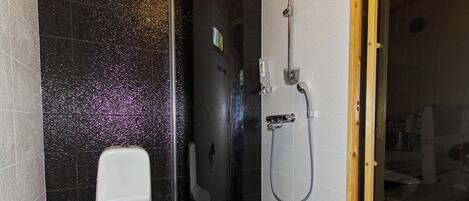 A bathroom with a white toilet, a shower area, and a tiled floor.