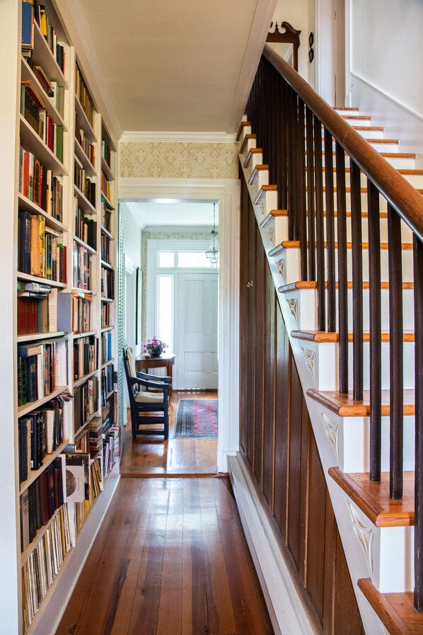 A narrow hallway with wooden bookshelves on one side and a wooden staircase on the other.