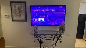 Ett vardagsrum med en platt-TV som är monterad på väggen, en inramad tavla ovanför och ett soffbord i glas med en metallram.