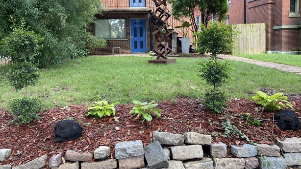 En bostadsfastighet med ett hus i tegel, en blå dörr och en trädgård med täckbark och växter.