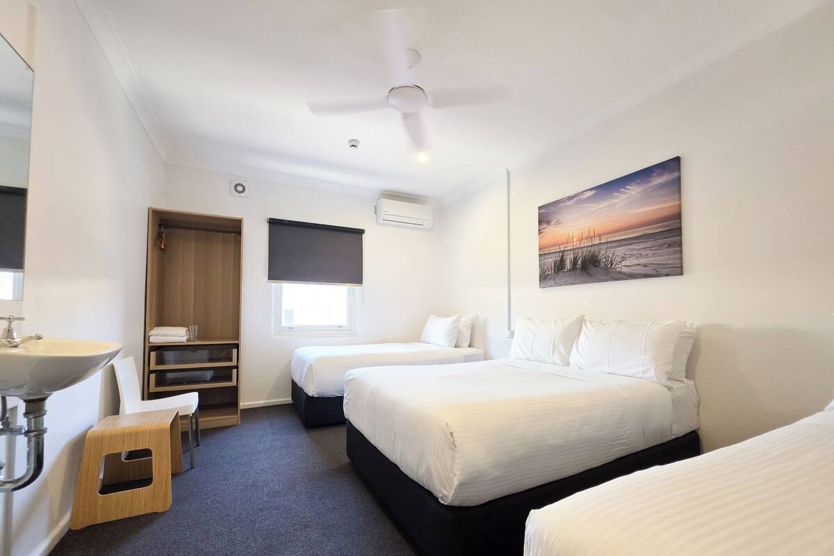 Habitación de hotel con dos camas, un baño con lavamanos y un ventilador de techo.
