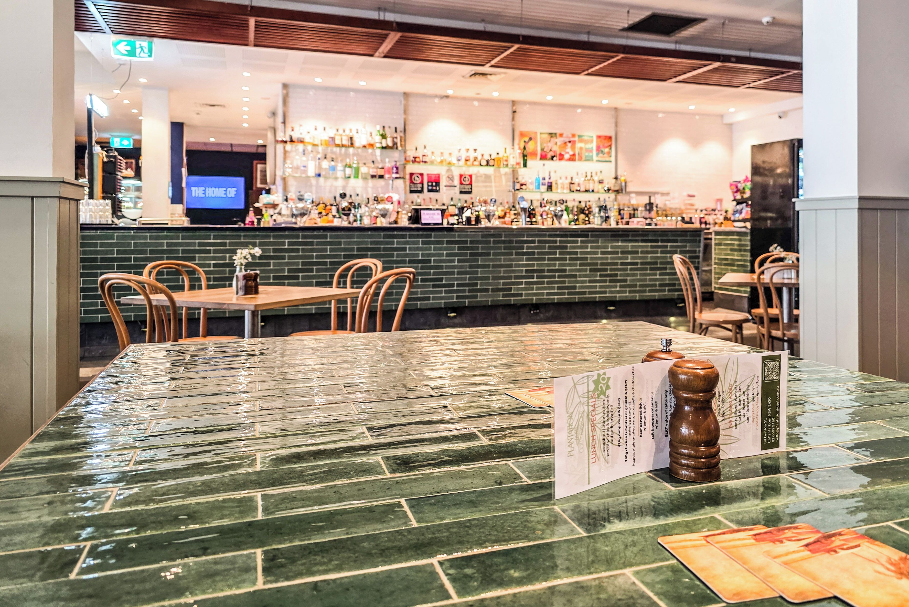 A restaurant with a green-tiled bar area, wooden chairs, and a menu stand.