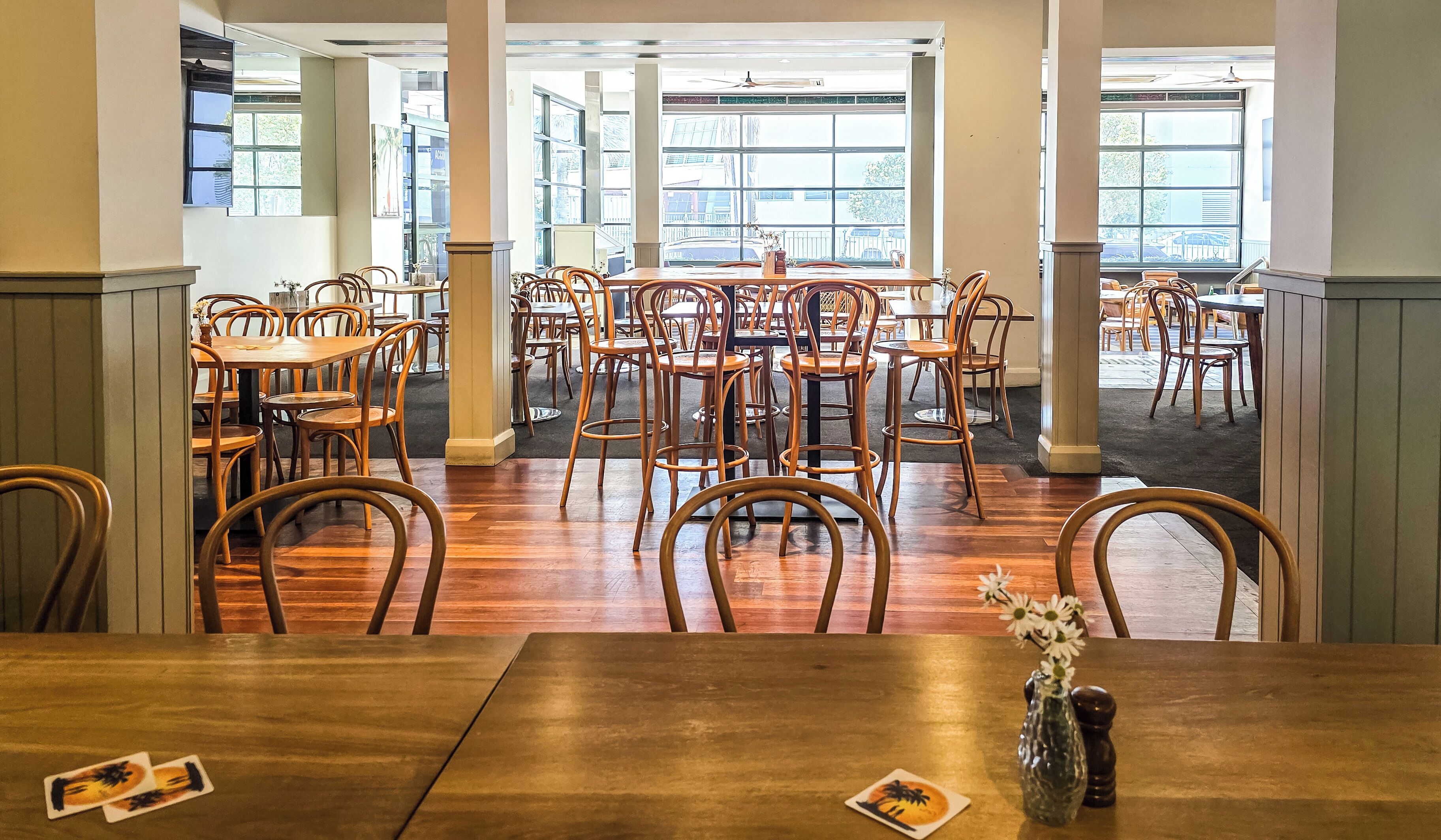 A spacious dining area with wooden tables and chairs, large windows offering views of the street, and a modern interior design.