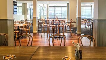 A spacious dining area with wooden tables and chairs, large windows offering views of the street, and a modern interior design.
