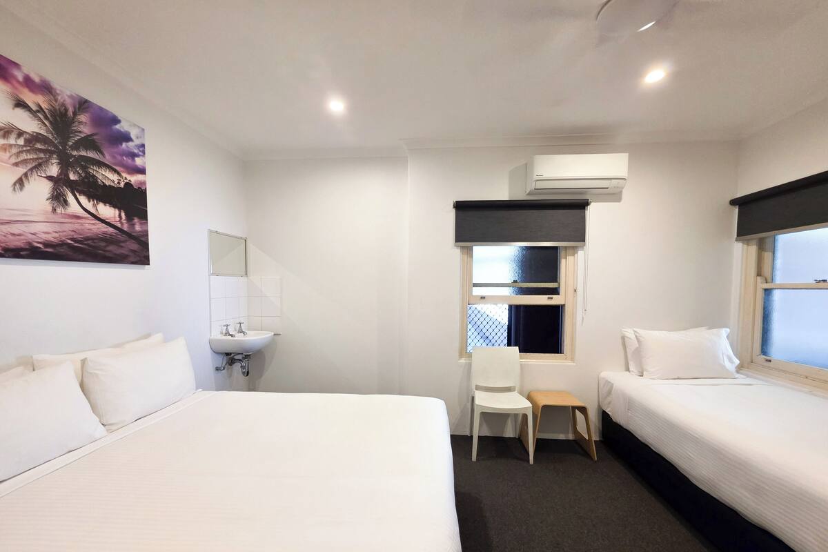 Habitación de hotel con dos camas, un lavamanos, una silla y una ventana con vistas.