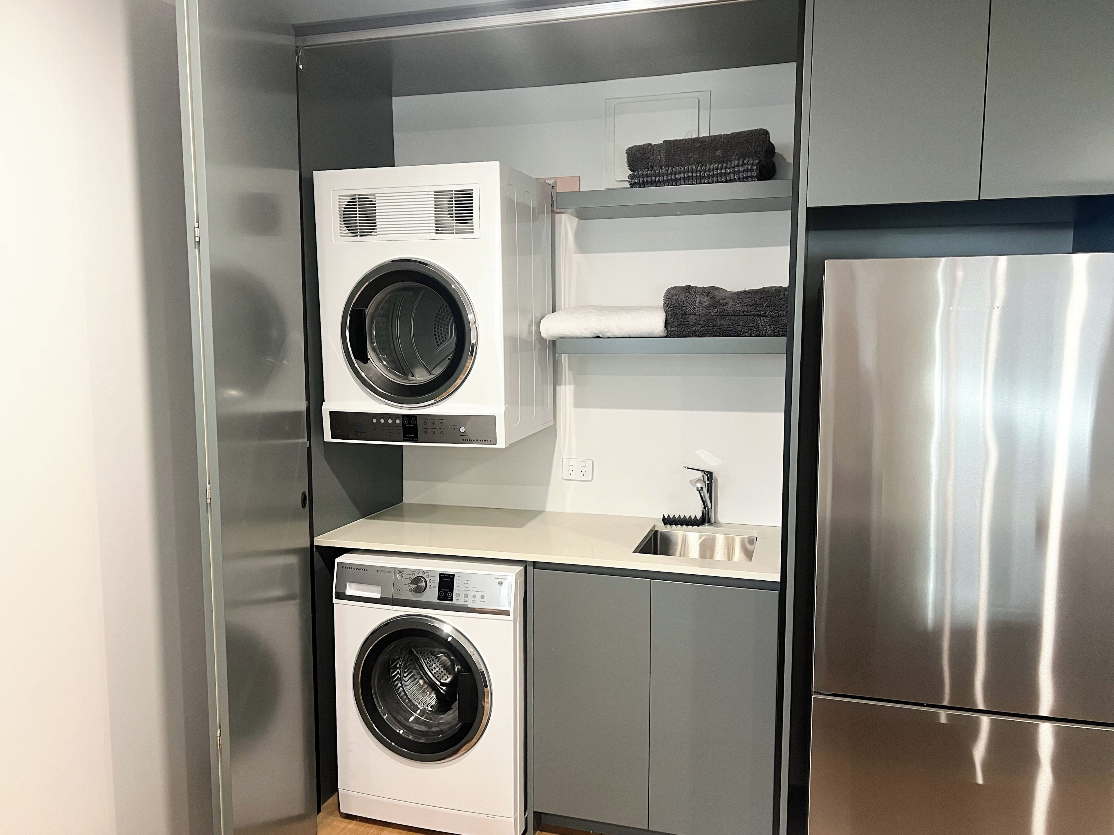 A compact kitchen with a stainless steel refrigerator, a built-in washing machine, and a sink.