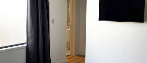 A hotel room with a bed, a TV mounted on the wall, a window with curtains, and a door leading to another room.