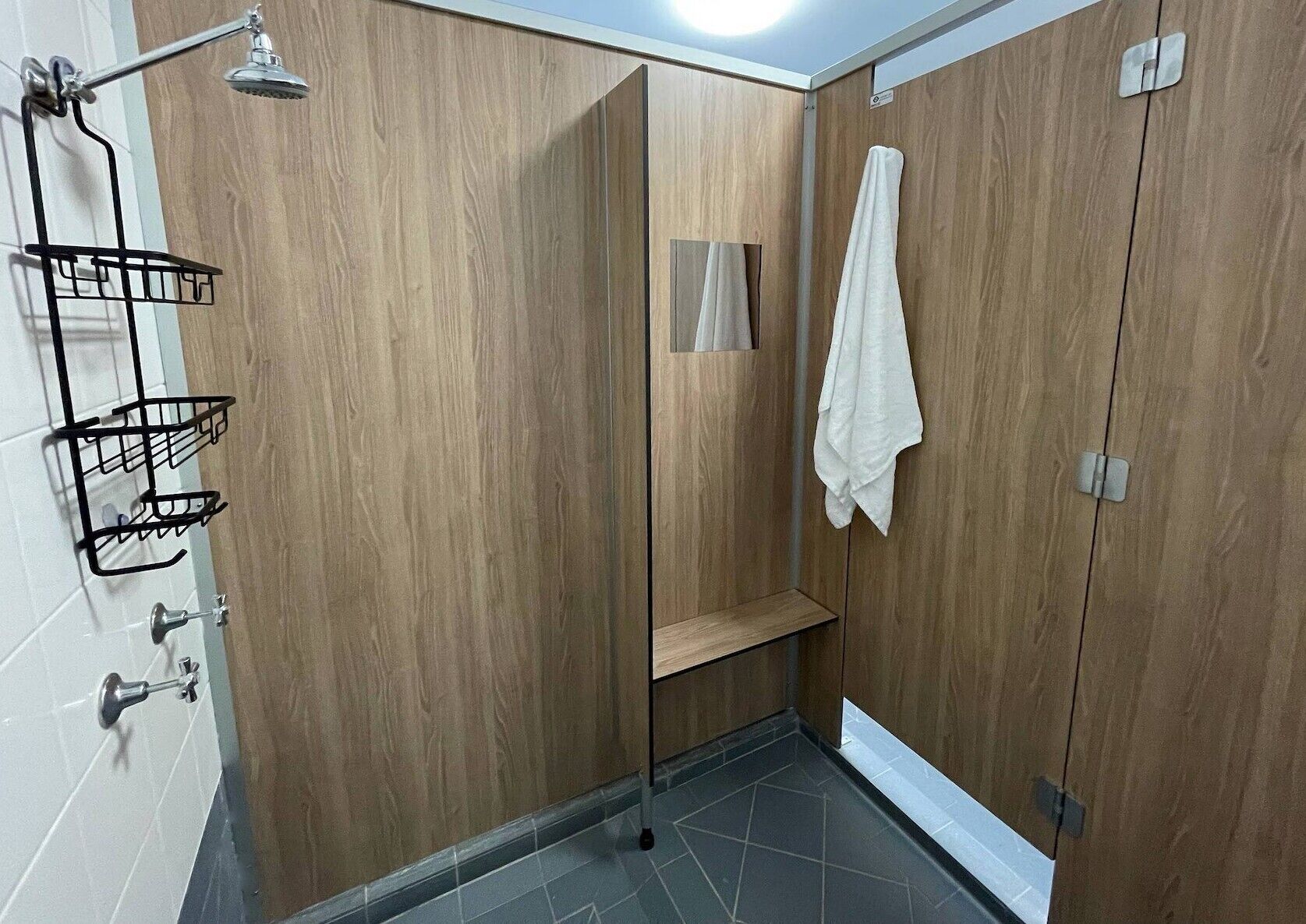 Een moderne badkamer met houten lambrisering, een douche met handdouche, een handdoekhouder en een klein plankje.