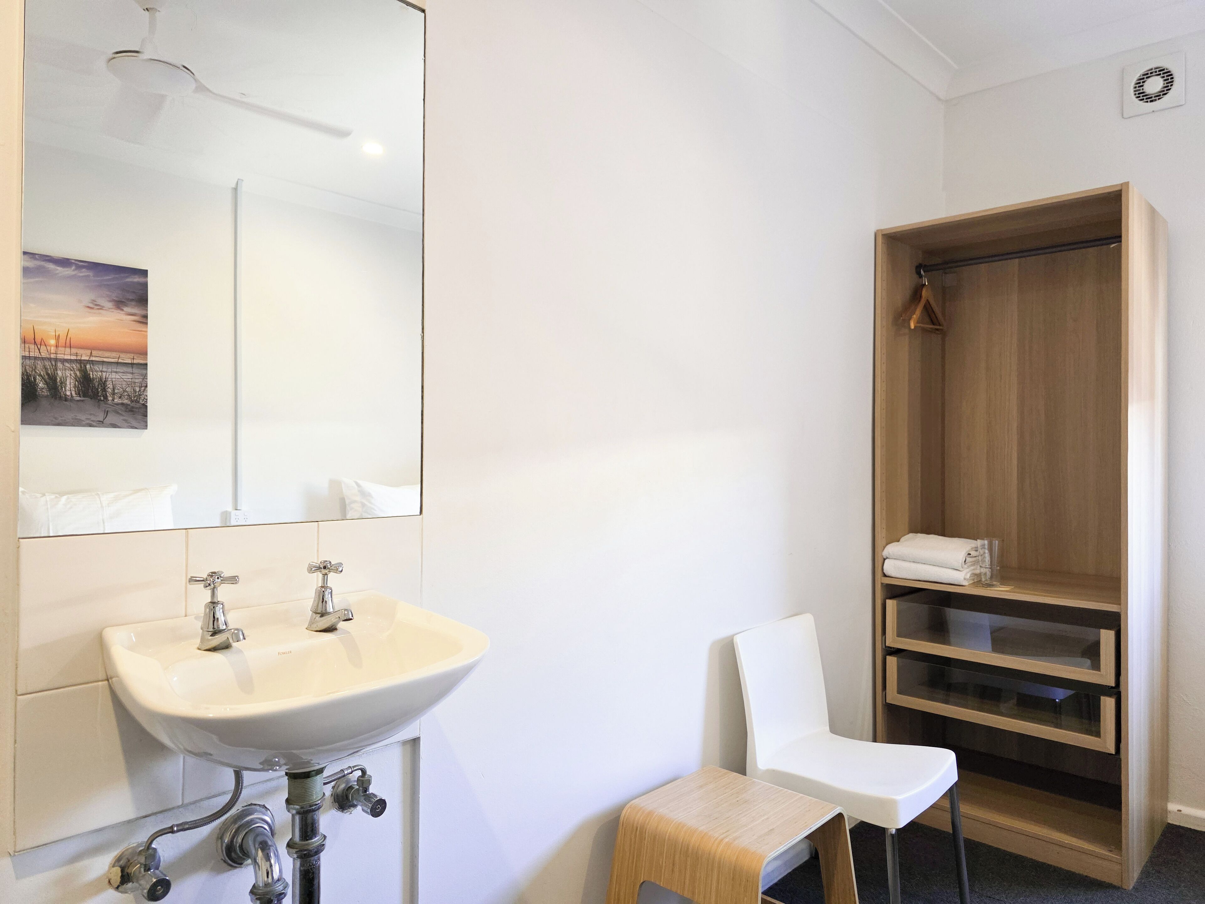 Un baño con lavamanos blanco, espejo y mueble de almacenamiento de madera.