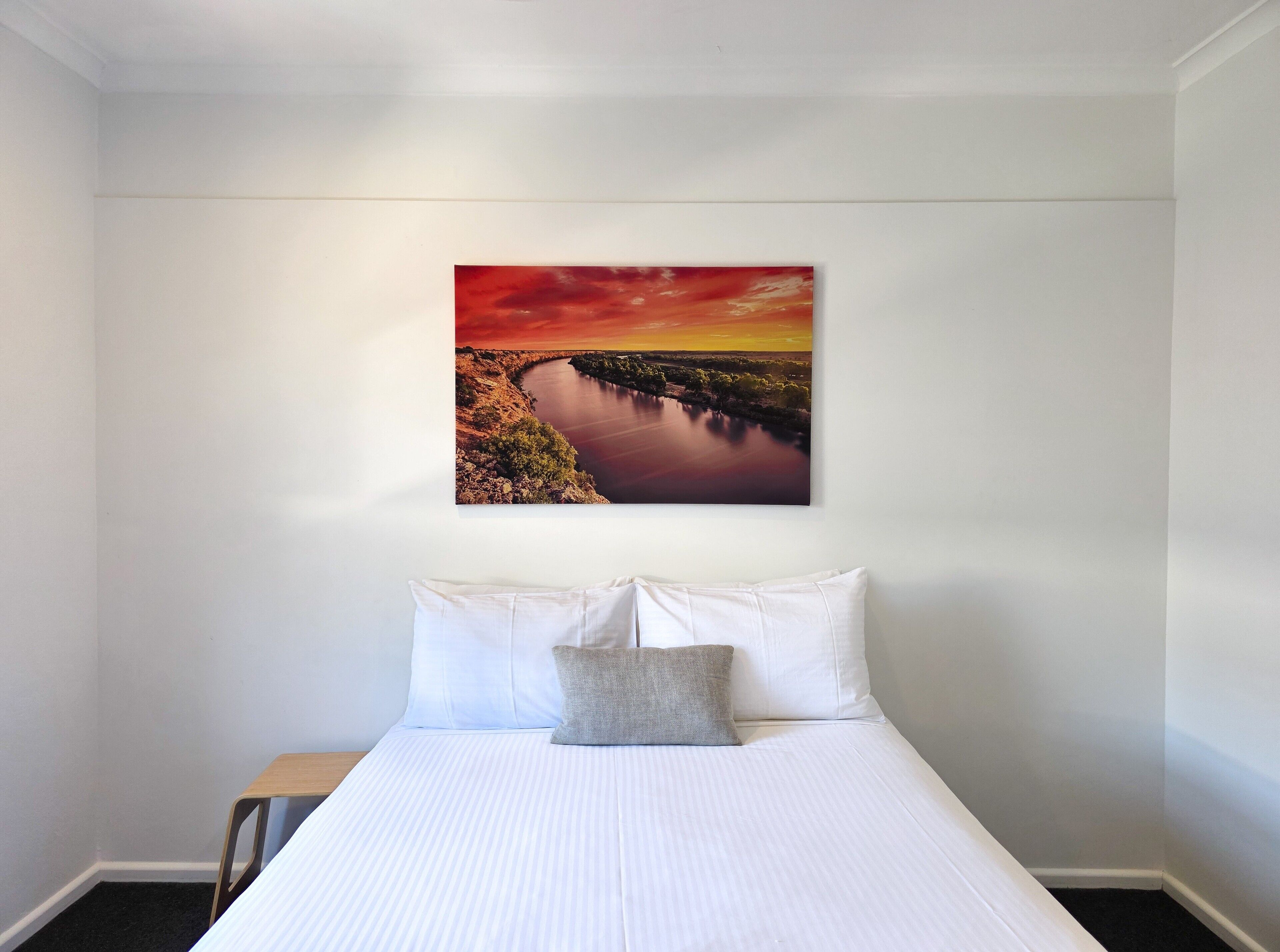 Un dormitorio con cama, almohadas y un cuadro de paisaje enmarcado en la pared.