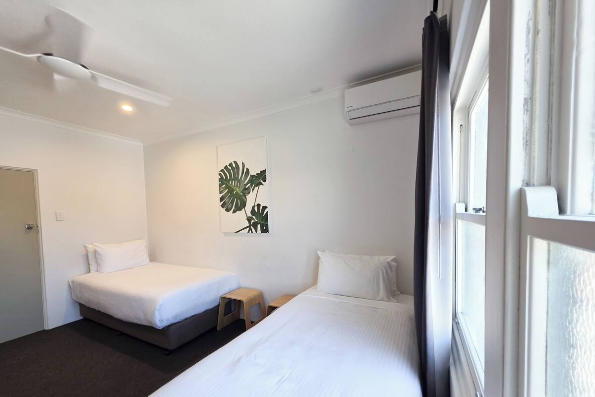 Habitación de hotel con dos camas, ventilador de techo, aire acondicionado y ventana con cortinas.