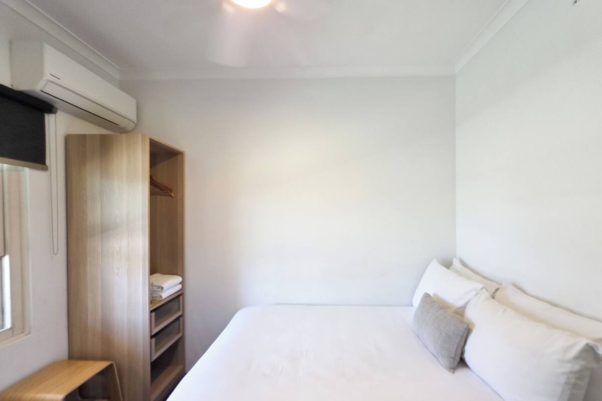 Un dormitorio con cama, armario de madera, escritorio y equipo de aire acondicionado.