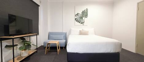 Un dormitorio con una cama, un televisor sobre un mueble bajo, una silla y un ventilador de techo.