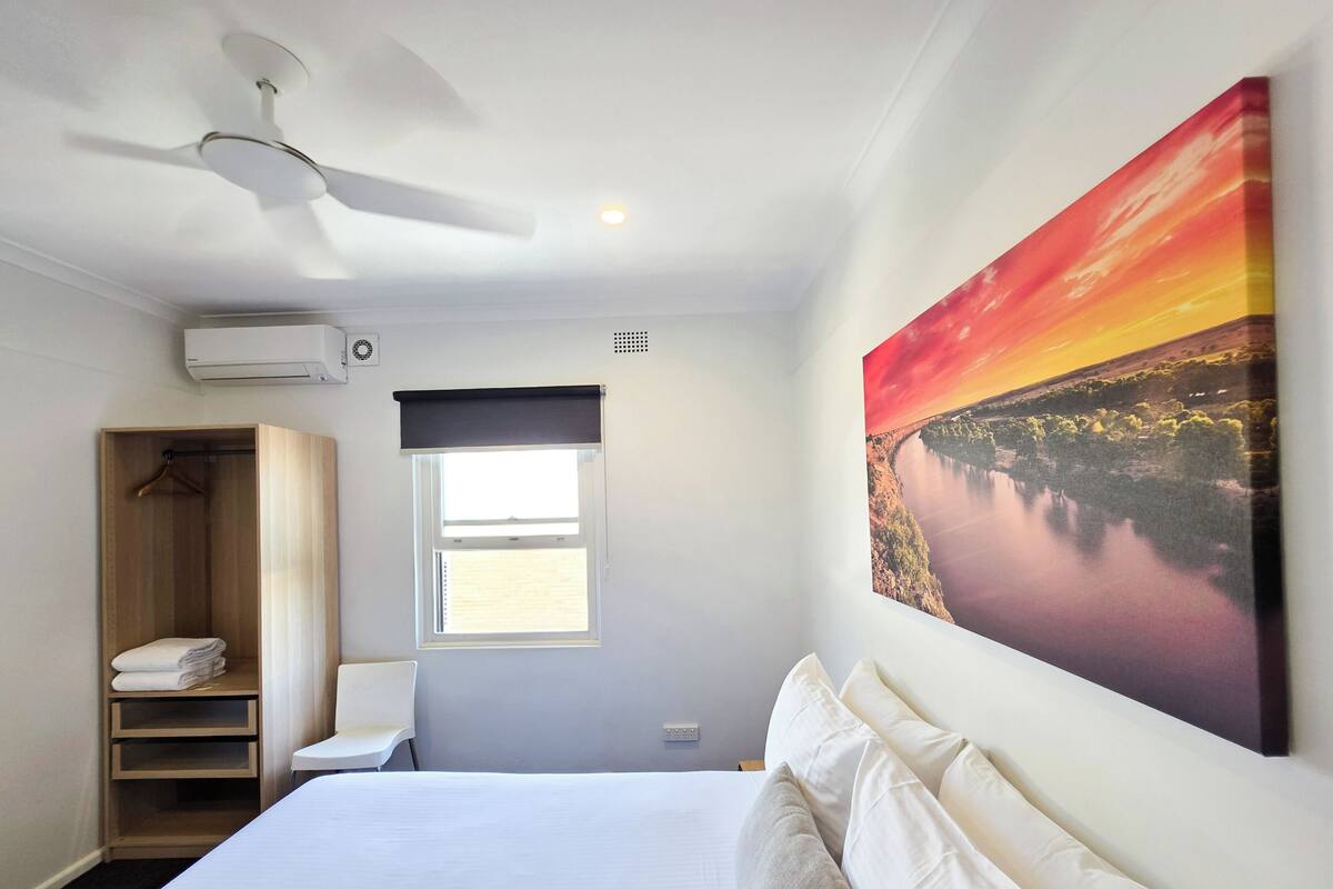 Una habitación de hotel con cama, armario, ventana y ventilador de techo.