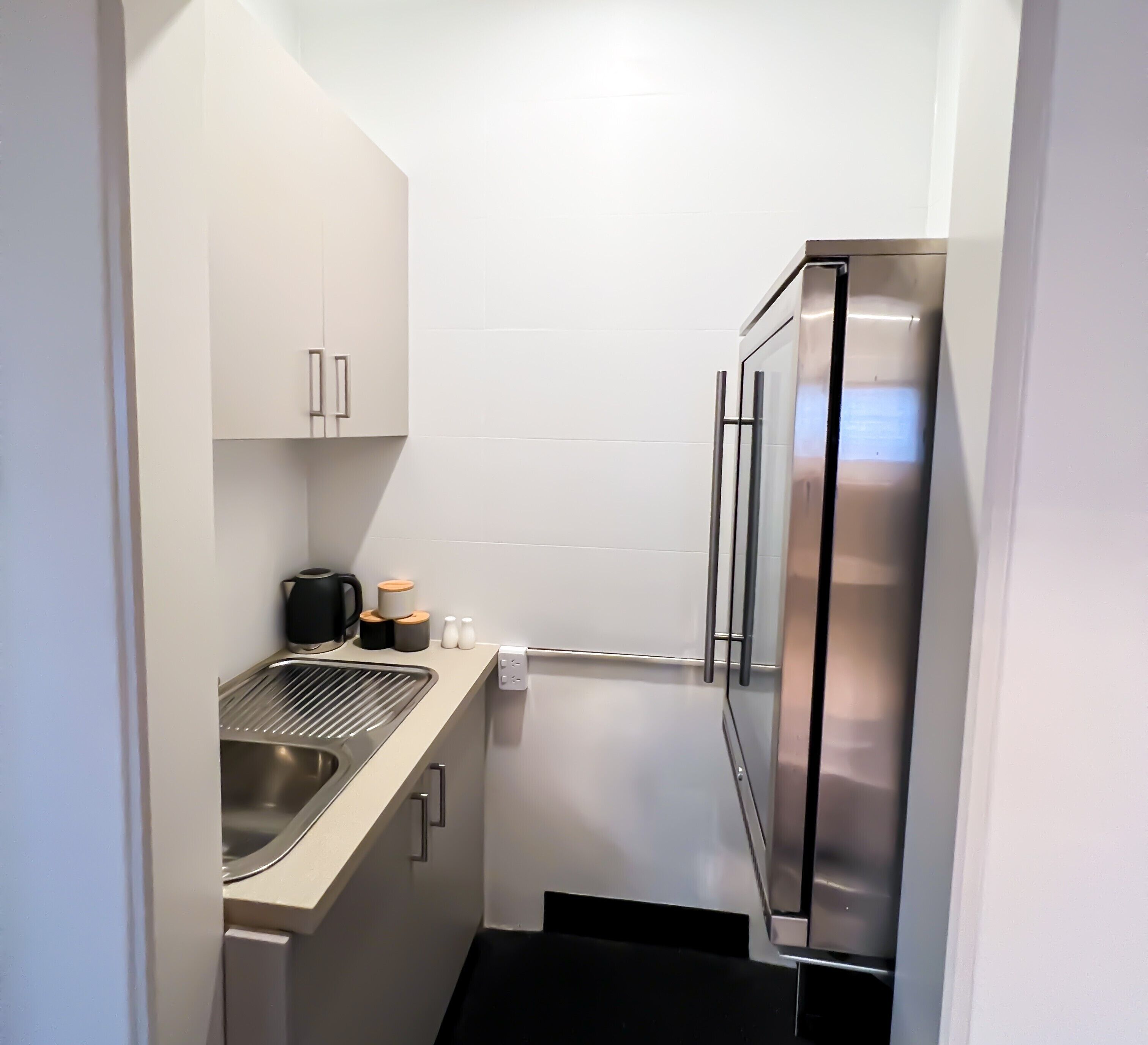 A compact kitchen with a stainless steel refrigerator, a sink, and a coffee maker.