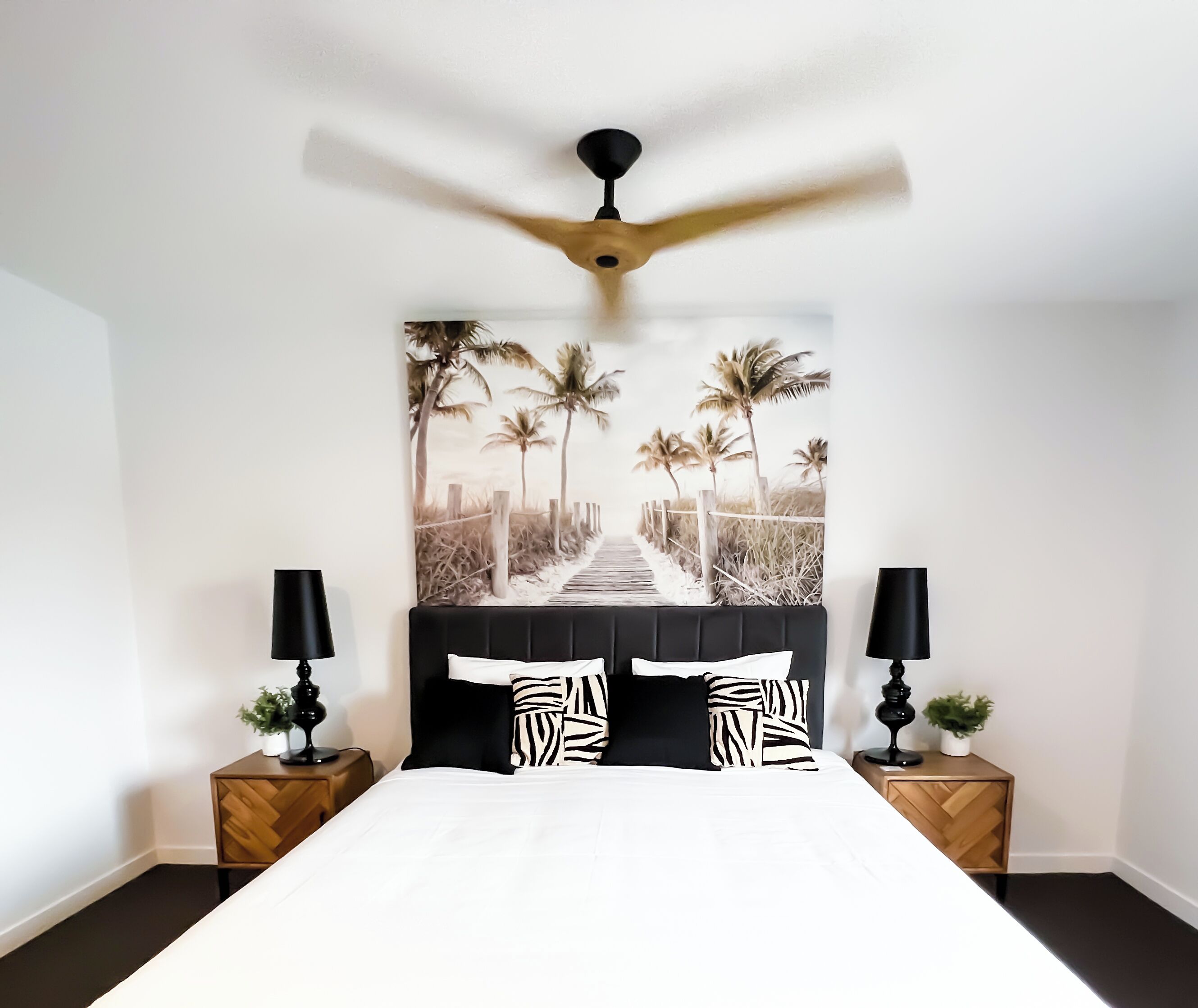 Un dormitorio con una cama, dos mesitas de noche, un ventilador de techo y una decoración de pared con temática playera.