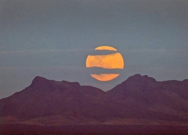 A mountain range with a large, orange moon reflecting on a body of water. - Desert Oasis "Cactus" Cabin (McNeal)