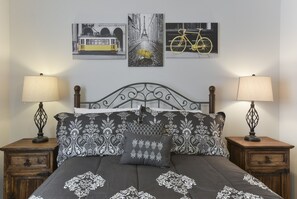 Un lit recouvert d’une couvre-lit à motifs noir et blanc, deux tables de chevet avec des lampes et trois tableaux encadrés accrochés au mur.