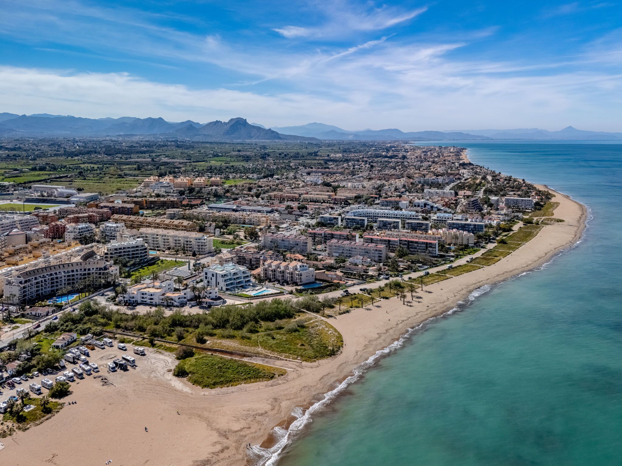Luftaufnahme einer Küstenstadt mit einem Hotelbezirk am Strand, der mehrere Hotelgebäude, einen Sandstrand und einen klaren Blick auf das Meer und ferne Berge zeigt.