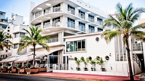 A modern hotel with multiple balconies, large windows, and a red-paved street in front.