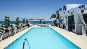 A pool area with a clear view of the sea, a white fence, and a building with colorful patterns.