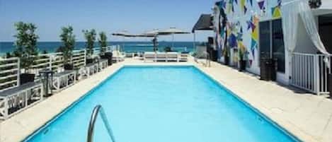 A pool area with a clear view of the sea, a white fence, and a building with colorful patterns.