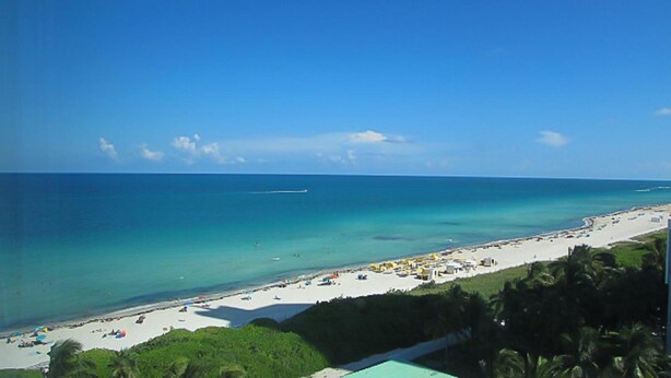 A beach with clear turquoise water, a sandy shore, and a few umbrellas.