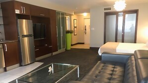 A modern living room with a leather sofa, a glass coffee table, and a kitchen area with a stainless steel refrigerator.