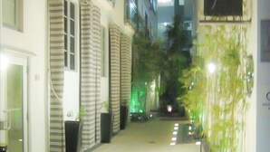 A narrow, well-lit corridor with a sign reading "1052 Strand" and a small outdoor area with plants and a water feature.