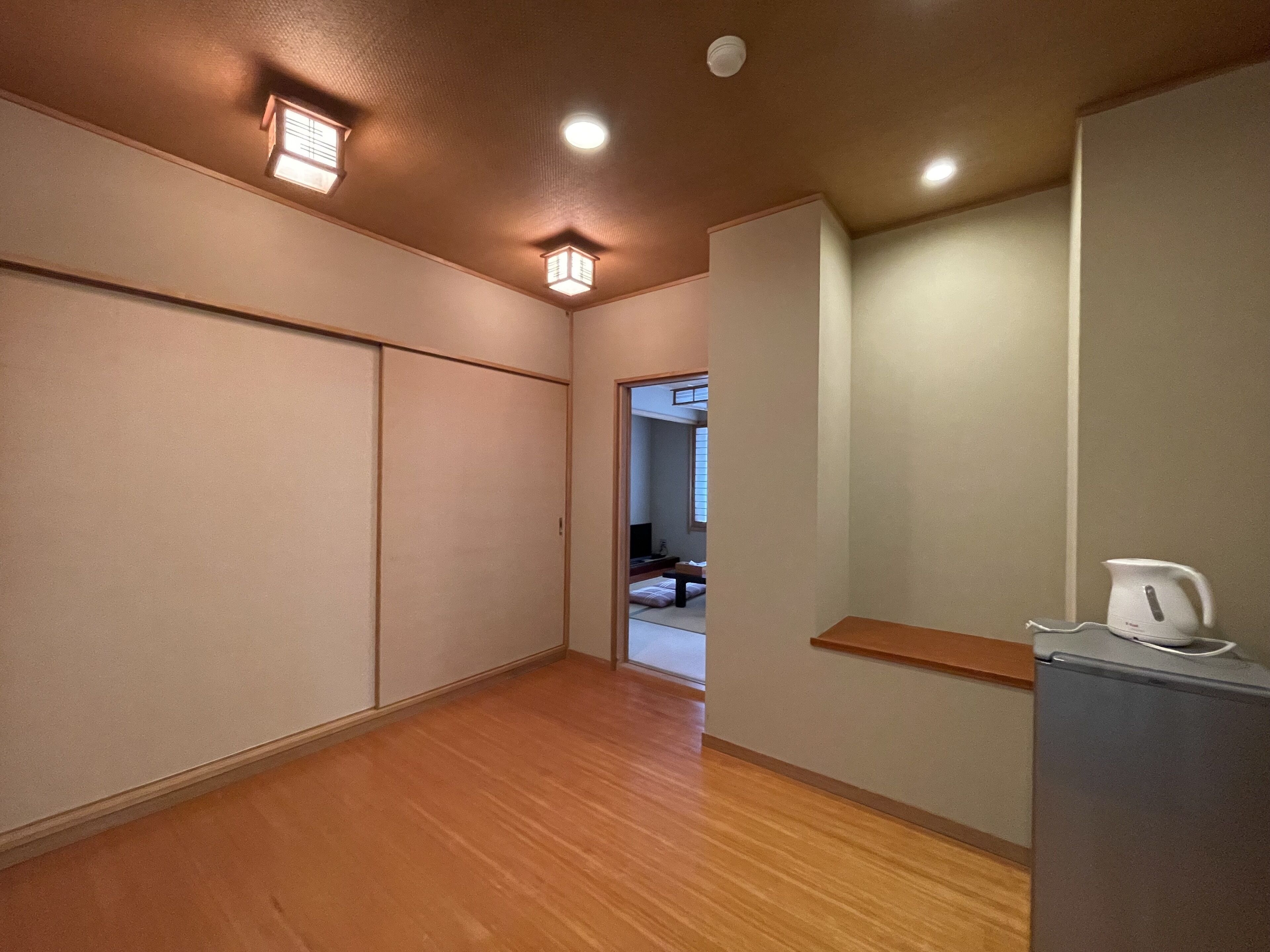 Un pasillo con puertas correderas, suelo de madera y una zona de kitchenette con refrigerador y hervidor.